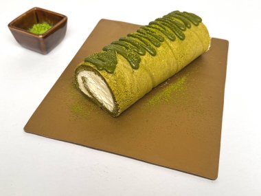 Kremalı kibrit yeşil çay rulo keki, üzeri kibrit jöleli ve kahverengi çarşafta toz çayla kaplı. Yiyecek fotoğrafçılığı kullanımı için yumuşak arkaplan ve sığ alan derinliği.