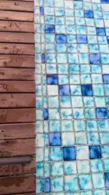 Mavi mozaik havuz fayanslarının yanında yumuşak su dalgaları olan ıslak ahşap döşemeleri gösteren dikey görüntüler. Yaz, tatil, spa ya da sağlık konularına uygun temiz bir arkaplan.