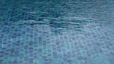 Mavi mozaik fayansların üzerinde hafif dalgalanmalar olan sakin yüzme havuzu görüntüsü, rahatlatıcı soyut bir arkaplan yaratıyor. Yaz, sağlık, tatil beldesi ve lüks kavramlar için ideal temiz, ferahlatıcı bir doku..