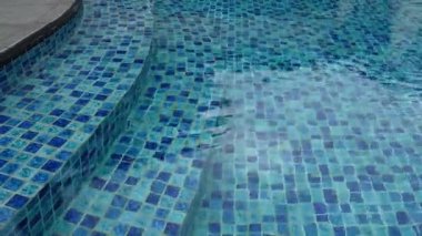 Mozaik fayans basamaklarının üzerinde hafif dalgalanmalar akan berrak mavi yüzme havuzu görüntüsü. Yaz, tatil, spa ve lüks eğlence kavramları için uygun soyut arka plan dinlendirici.