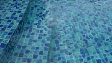 Mozaik fayans basamaklarının üzerinde hafif dalgalanmalar akan berrak mavi yüzme havuzu görüntüsü. Yaz, tatil, spa ve lüks eğlence kavramları için uygun soyut arka plan dinlendirici.