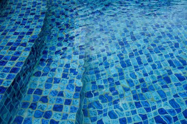 Mavi mozaik fayanslı ve hafif dalgalı soyut yüzme havuzu su dokusu. Kopya alanı olan temiz yaz arkaplanı, seyahat, tatil yeri, rahatlama ve tasarım kavramları için ideal.