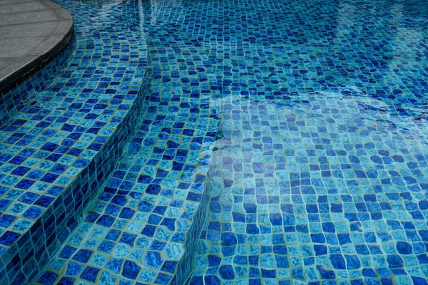 Mavi mozaik fayanslı ve hafif dalgalı soyut yüzme havuzu su dokusu. Kopya alanı olan temiz yaz arkaplanı, seyahat, tatil yeri, rahatlama ve tasarım kavramları için ideal.