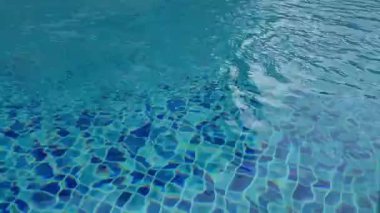 Temiz mavi yüzme havuzu görüntüsü, hafif dalgalar ve güneş ışığı yansımaları. Soyut sakin su dokusu yaz, refah, rahatlama, seyahat, lüks ve tatil beldeleri için idealdir..