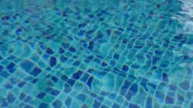 Temiz mavi yüzme havuzu görüntüsü, hafif dalgalar ve güneş ışığı yansımaları. Soyut sakin su dokusu yaz, refah, rahatlama, seyahat, lüks ve tatil beldeleri için idealdir..