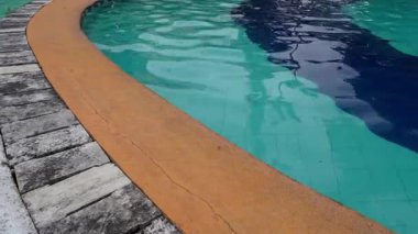 Kıvrımlı yüzme havuzu kenarı turkuaz su ve daha koyu mavi yansıma çizgisi. Modern bir açık hava tatil köyünde soyut su dalgalanmaları ve geometrik çizgiler.