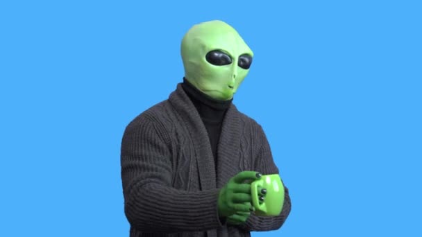 Hombre disfrazado de alienígena, abrigado chaqueta de punto, con divertida taza temática en la mano se ríe, se retuerce de risa, contra una llave de croma azul. Preparación para la fiesta de Halloween — Vídeo de stock