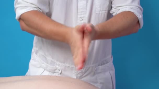 Gros plan mains de massages masculins vêtus d'un manteau blanc, balayant précieusement l'huile spéciale et commençant à faire le massage du patient, couché sur le canapé — Video