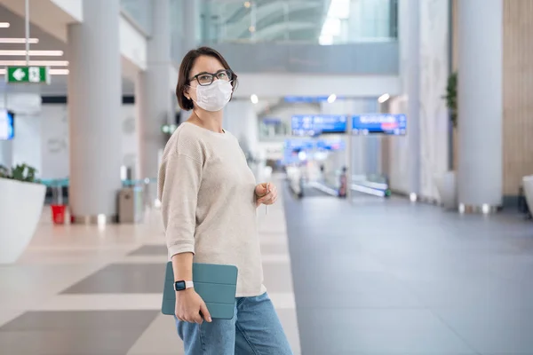 Joven mujer feliz con máscara respiratoria médica protectora y tableta digital va a registrarse para el vuelo antes de irse de vacaciones. Nueva vida durante la pandemia —  Fotos de Stock