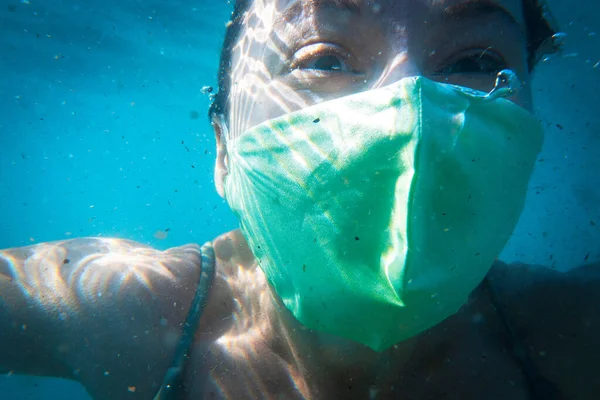 Joven mujer activa en máscara médica protectora se dedica a bucear y nadar bajo el agua, vista frontal, de cerca. Bromas sobre la nueva vida durante la pandemia —  Fotos de Stock