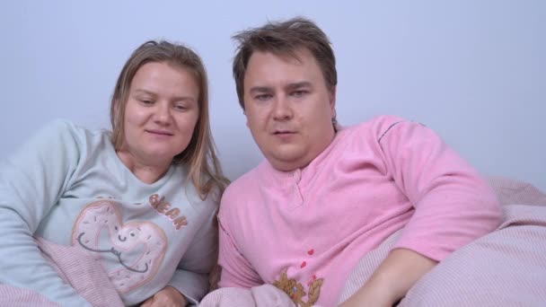 Young married couple wearing pajamas is lying in bed and looking around in surprise. They look at each other questioningly, man shrugs, and they leave to check what is going on — Stock Video