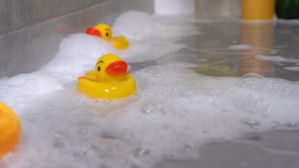 Spielzeug-Gummi-Enten schwimmen in seifigem Wasser auf Fliesenoberflächen in der Dusche. Dicker Schaum kommt immer mehr an und überflutet Spielsachen. Unterhaltung für Kinder beim Baden — Stockvideo