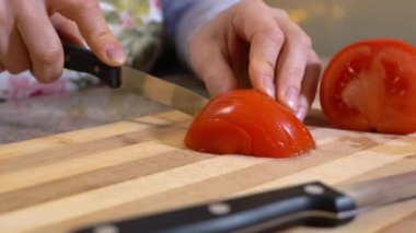 Çiçekli önlüklü bir insan salata ya da vejetaryen yemeği hazırlamak için domatesi ince dilimlere ayırır. Bir yemek programının reklamı.