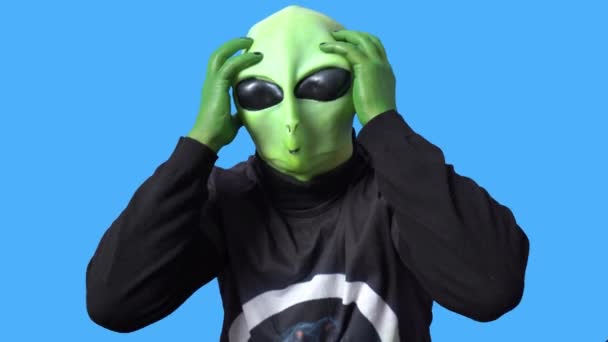 Artista profesional en traje alienígena y en una camiseta negra se ríe y se agarra la cabeza en la histeria contra el fondo azul cromakey. — Vídeo de stock