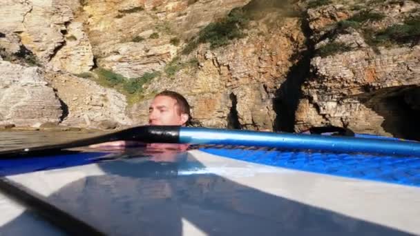 Trött ung man försöker komma ur havet eller havet på SUP styrelse, kisar och torka ögonen och ansiktet från vatten, sidovy. Fall och misslyckanden i extrema sporter — Stockvideo