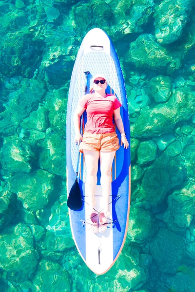 Mujer se encuentra en una tabla de paddle y disfruta de la recreación al aire libre. Deportes activos, salud mental. Interesante hobby mientras está de vacaciones —  Fotos de Stock