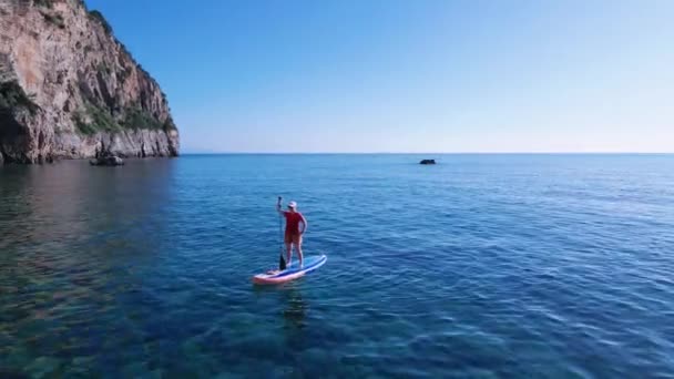 Jeune femme en casquette et lunettes de soleil se tient sur SUP board avec pagaie à la main. Tir avec drone volant autour de la personne. Loisirs actifs et mode de vie sain