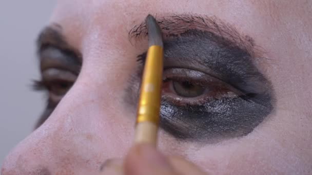 Artista de maquillaje profesional aplica maquillaje negro inusual a los ojos de la actriz para rodar escena de película de terror o producción teatral. — Vídeo de stock