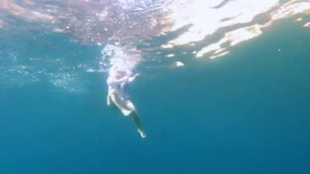 Junge Frau in zweiteiligem Badeanzug und weißem Hemd schwimmt im Meer, jemand spioniert sie heimlich unter Wasser aus, schießt auf Actionkamera, Ansicht von unten — Stockvideo