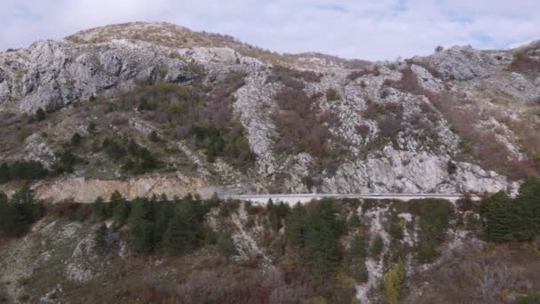 Tiro con drone dall'alto guida vista sulla stretta autostrada. Bella vista delle montagne coperte di foresta sparsa ed erba secca in autunno. — Video Stock