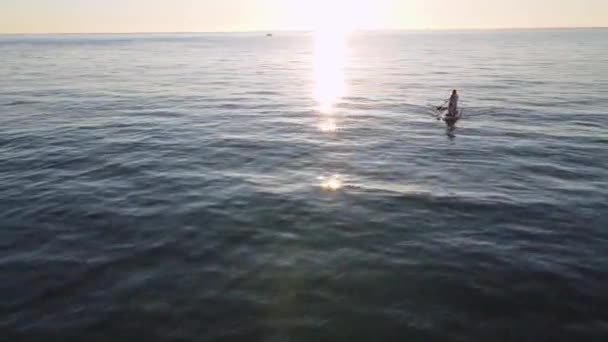 Mulher loira desportiva está ajoelhada na placa SUP e remo com remo flutuando para a costa, drone atirando de altura, — Vídeo de Stock