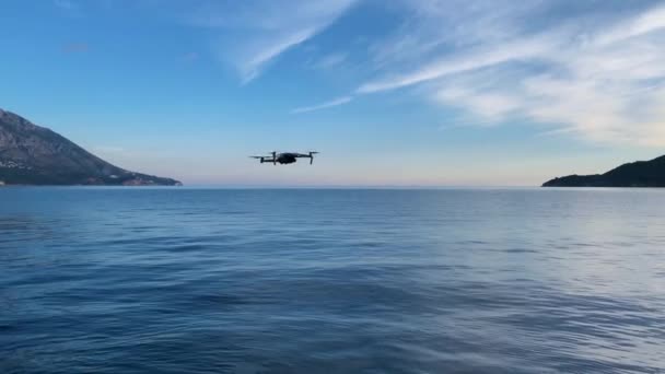 Drone flotó por un momento sobre la calma, superficie reflejada de agua y voló a la distancia para tomar fotos o video de hermosos paisajes marinos con montaña — Vídeo de stock