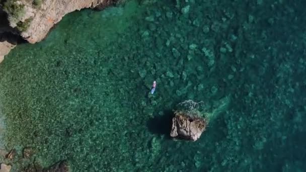 Jeune homme athlétique se trouve sur la planche SUP avec la main derrière la tête et frissons au soleil pendant les vacances, prise de vue avec drone de hauteur, zoom avant, vue du dessus. — Video