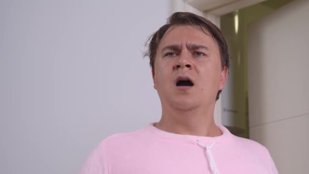 Przystojny mężczyzna w różowej piżamie krzyczy z otwartymi ustami, przerażony czymś w domu. — Wideo stockowe