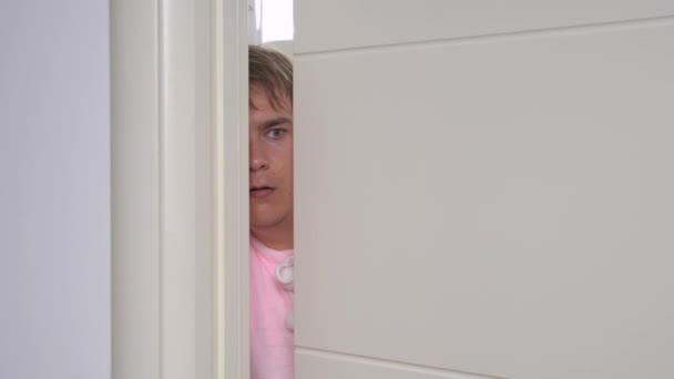 Vyděšený mladý muž se dívá skrz dveře rozdělené na padající oblečení — Stock video