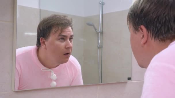 Νεαρός άνδρας με ροζ πιτζάμες πλένει το πρόσωπό του στο μπάνιο το πρωί αφού ξυπνήσει ή το βράδυ πριν πάει για ύπνο. Παράξενος δυνατός ήχος τράβηξε την προσοχή του άντρα — Αρχείο Βίντεο