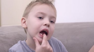 Komik küçük çocuk kanepede alt çene kemiğinde süt dişini gevşetiyor.