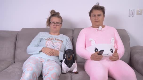 Bestört kvinna och man i pyjamas med tax valp titta på — Stockvideo