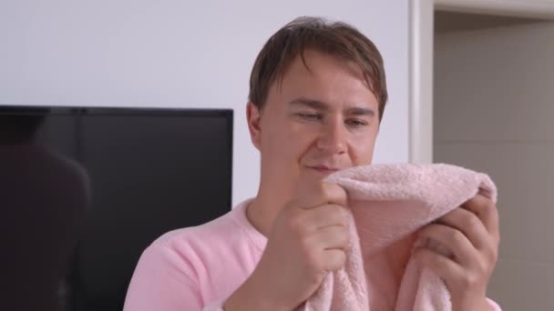 Νεαρός άνδρας με ροζ πιτζάμες με πομπόν εξετάζει νέα πετσέτα μπάνιου που αξιολογεί την ποιότητα και γνέφει θετικά δείχνοντας αντίχειρες επάνω χειρονομία πριν από τη λήψη ντους στο σπίτι ή στο ξενοδοχείο — Αρχείο Βίντεο