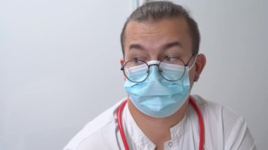Şok olmuş doktor, gözlüklü ve maskeli el sallıyor.