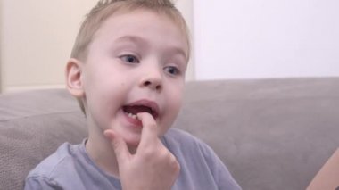 Bebek dişlerinin azı dişlerine çevrilmesi. Küçük çocuk yüzünü buruşturur ve ağzındaki eliyle gevşek dişlere dokunur. Çocuk diş perisinden hediye almak istiyor.