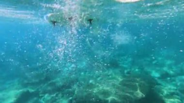 Çağdaş SUP sörf tahtasının sualtı görüntüsü kayalık dipteki sakin mavi deniz suyunda yavaşça süzülüyor..