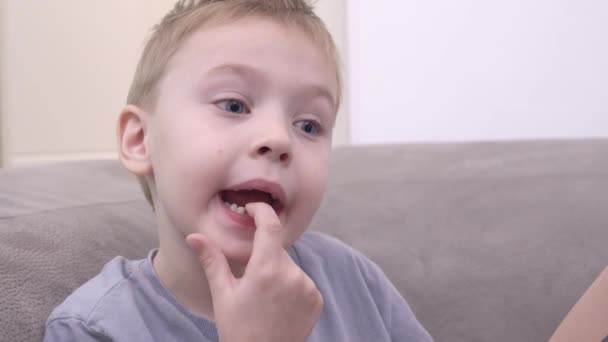 Cambio de dientes de bebé a molares en el niño. El niño hace la cara y toca los dientes sueltos con la mano en la boca. El chico quiere un regalo del hada de los dientes. — Vídeo de stock