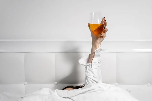 Woman is lying in bed raising hand holding glass filled with drink. Carefree and irresponsible life. Psychological problems or life difficulties that person tries to solve with alcohol — Stock Photo, Image