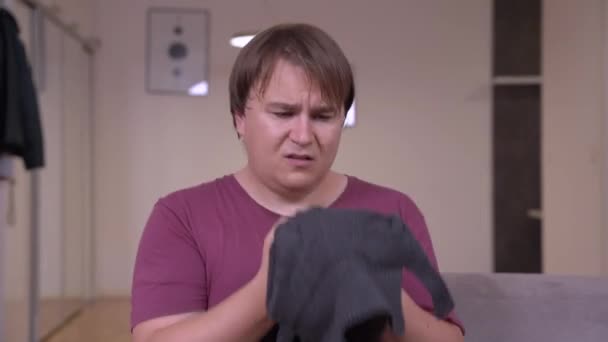 Αναστατωμένος άνθρωπος με υπέρβαρο κοιτάζει μικρό μέγεθος σακάκι στον καναπέ — Αρχείο Βίντεο