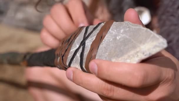 Caveman faz ferramenta de caça de pau de madeira, pedra afiada e cadarços de couro, de perto. Homem prepara equipamentos para performance teatral ou reconstrução histórica antiga — Vídeo de Stock