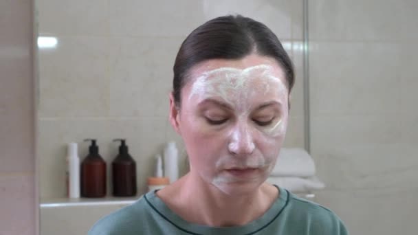Mladá žena si nanáší na obličej jílovitou čisticí nebo silně hydratační masku. Očista a hydratace pleti je nejdůležitějším stádiem každodenní péče o obličej — Stock video