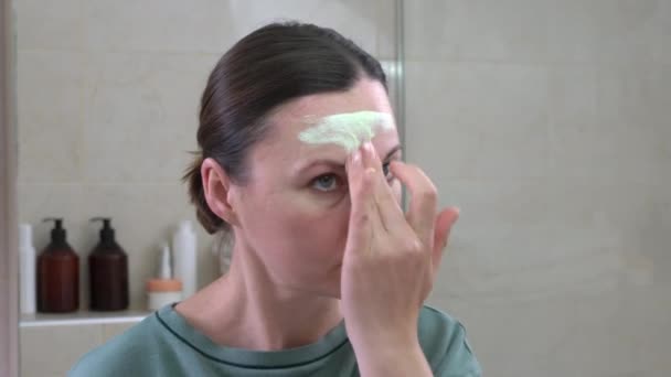 Mulher atraente aplica máscara verde no rosto perto do espelho — Vídeo de Stock