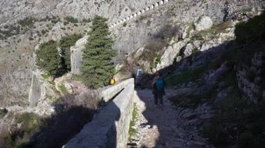 Turistler güneşli bir günde Kotor kalesinde patikadan aşağı iniyorlar
