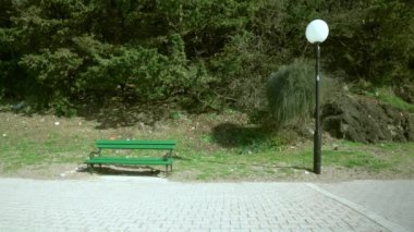 Tarzcı çizgili kazak ve kot pantolonlu genç bir kadın kayalık alelya boyunca yürür ve ılık bahar günü manzaralı saate bakar.