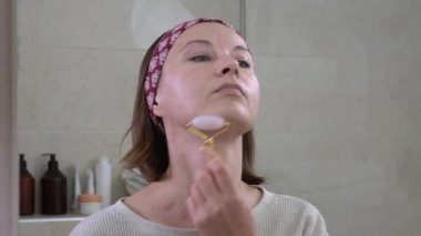 Genç bir kadın nemlendirici krem sürdükten sonra kuvars meso silindiriyle canlandırıcı ve pürüzsüz yüz masajı yapıyor. Kadınların günlük güzellik ritüelleri