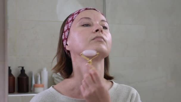 Jeune femme fait rajeunissant et lissant massage facial avec rouleau méso quartz après l'application de crème hydratante. rituels de beauté quotidienne des femmes — Video