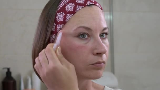 Досить короткошерста зріла дама використовує рожевий кварцовий інструмент для гоління для масажу зморшок лоба у легкій ванній крупним планом — стокове відео