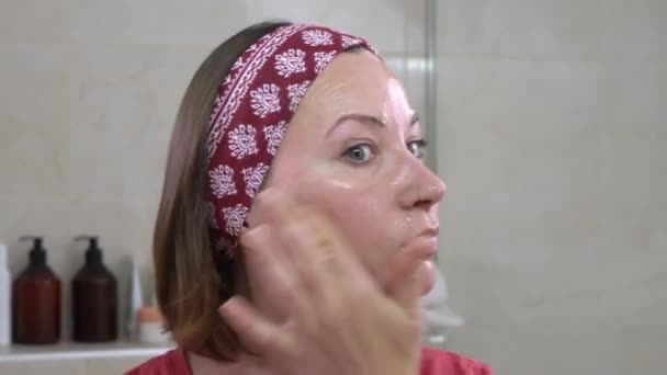 Belle jeune femme applique du sérum d'huile nourrissante ou un masque gel hydratant avec des oligo-éléments actifs sur son visage avec des mouvements de massage. rituels de beauté quotidiens et soins de la peau — Video