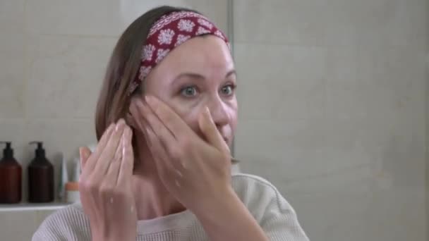 Mulher loira limpa o rosto com esfoliação olhando no espelho — Vídeo de Stock