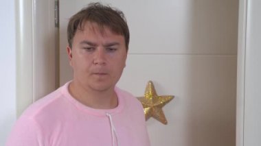 Pembe pijamalı genç baba bebeği yeni yatırmıştı. Öfkeli adam, yeni doğan bebeği uyandırmamak için el hareketleriyle hareket eder ve kontrol etmek için odaya bakar.
